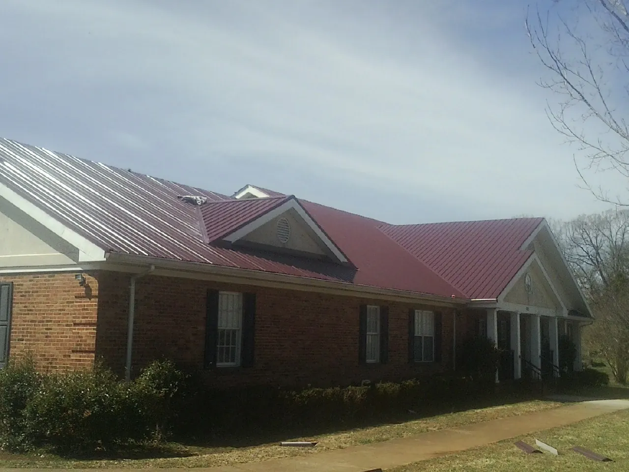 Red metal roof with gabled entries on a long brick building, from a Hail Damage Roof Repair job in Topping