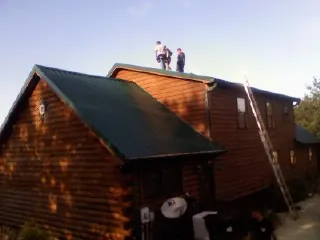 Crew on the ridge of a green metal roof on a two story log home in Topping