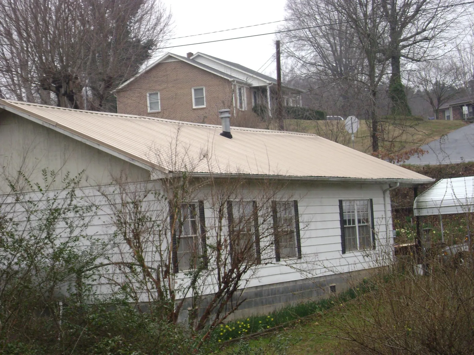 Tan metal roof on a white sided house set into a hillside — Commercial Roofing by Roofing Brothers in Topping