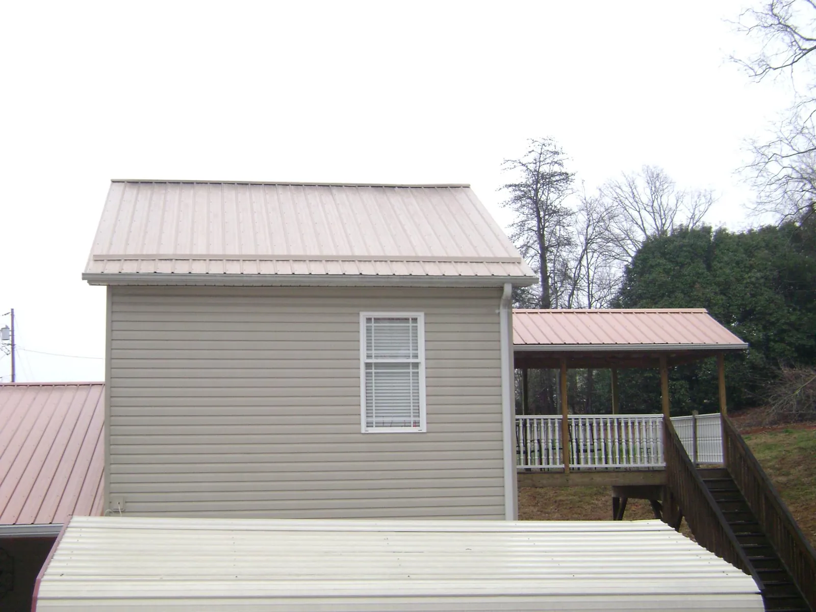 Tan metal roofs on a two story addition and attached porch, from a Roof Replacement job in Topping