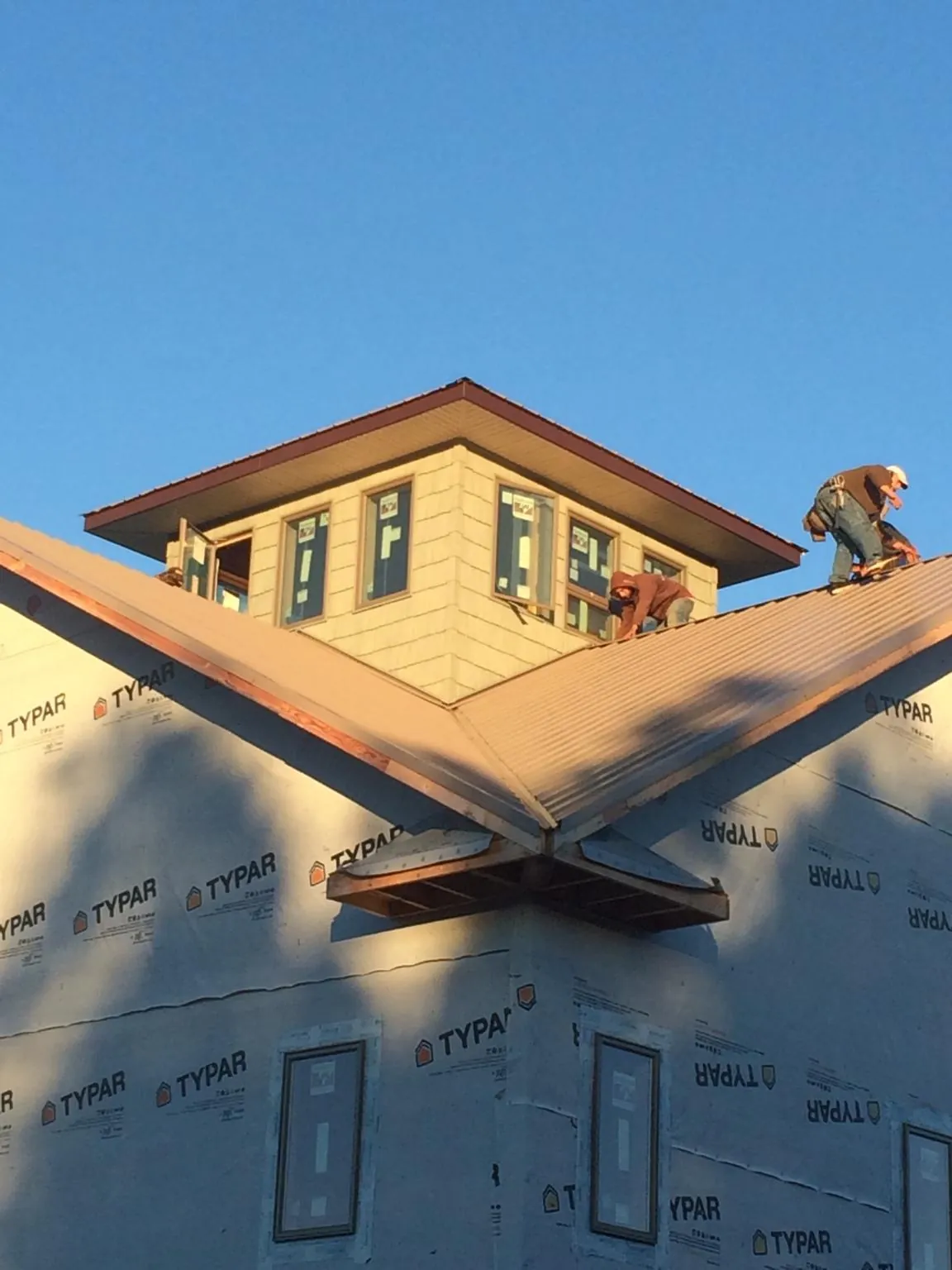 Roofers working around a rooftop cupola on a new metal roof at sunset — Roof Waterproofing in Topping by Roofing Brothers